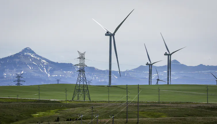 Wind turbines and transmission towers in a field with snowcapped mountains in the background