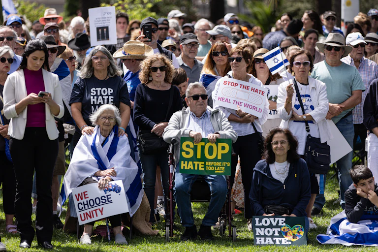 A crowd of protestors holding Israeli flags and signs that say stop the hate