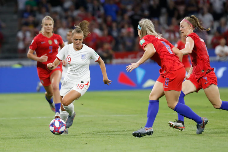 Team England player Georgia Stanway dribbles the ball while avoiding three opponents.