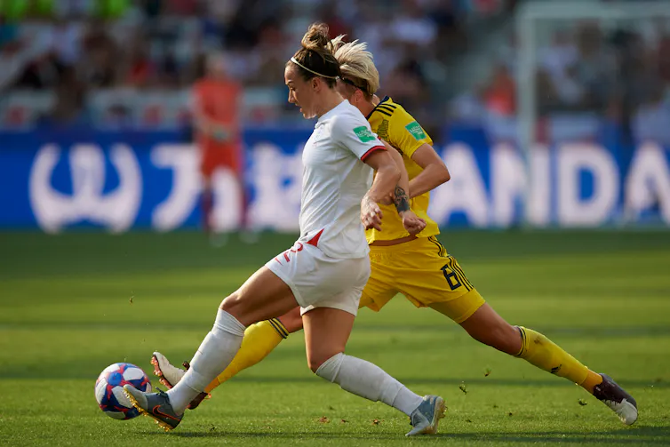 England footballer Lucy Bronze kicks the ball forward while holding off an opponent.