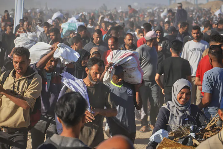 A huge crowd of Palestinian people carry their belongings along a dusty road.