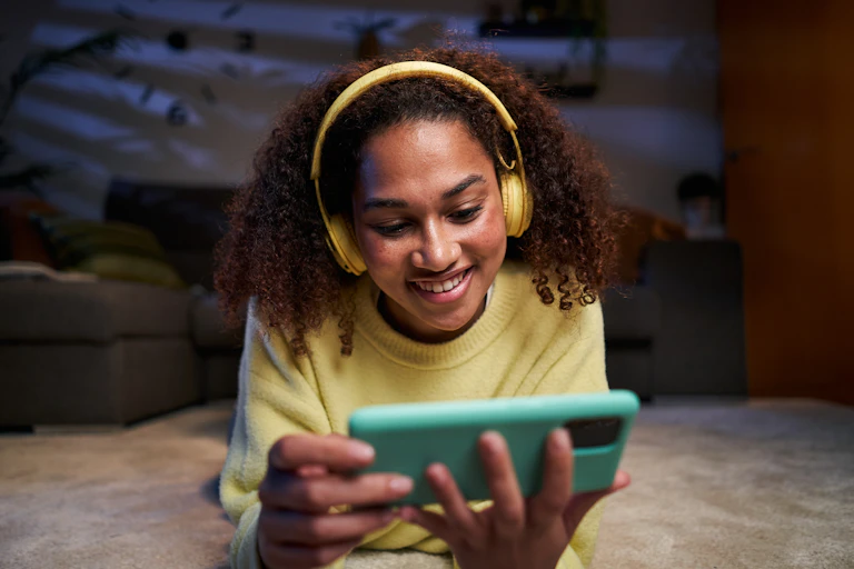 black woman wearing yellow headphones, watching music video on green phone
