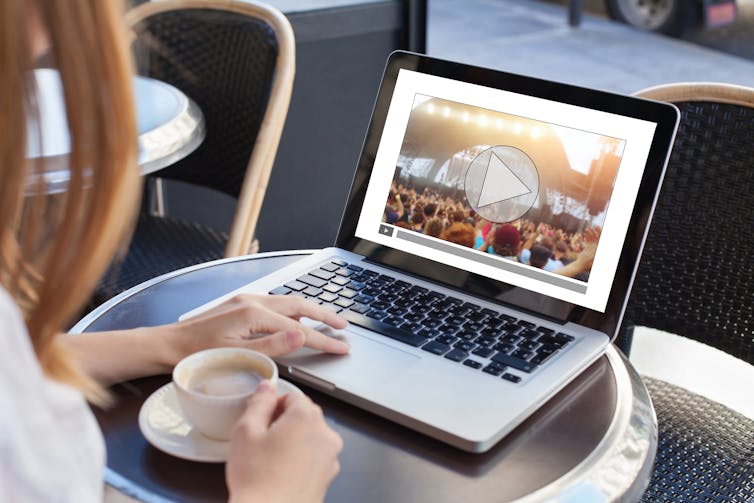 woman at cafe table with laptop open watching music video