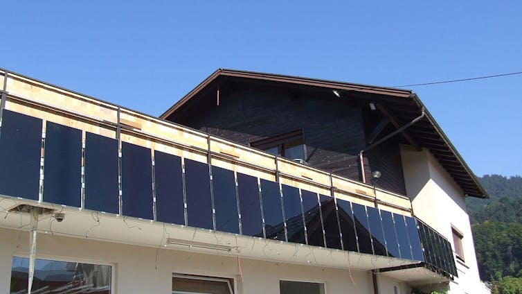 A house with a large balcony covered with a vertical line of panels.