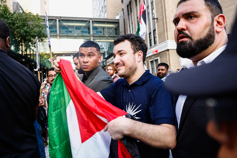 A man in a crowd holds a Palestinian flag