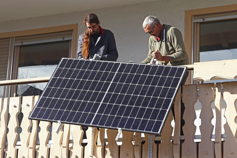 Two men lowering a solar panel over the edge of a balcony.