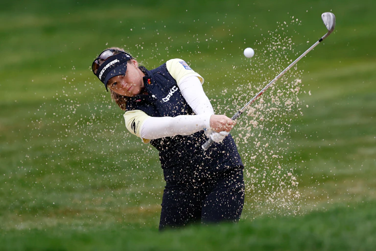 A woman hits a golf ball out of a sand trap on a golf course