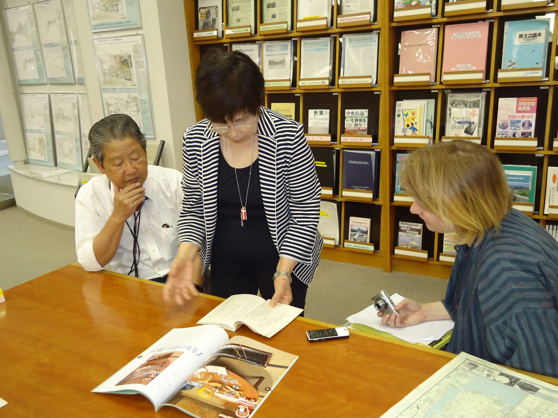 Three people look over books  in a library in Japan.