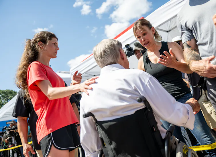 Surrounded by community members and volunteers, an emotionally distraught woman speaks to the governor of Texas.