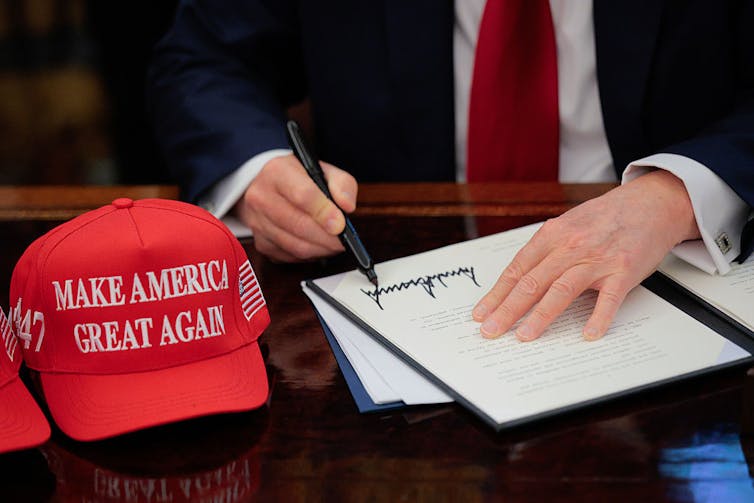 U.S. President Donald Trump signs an executive order with a 'Make America Great Again' hat near the document.