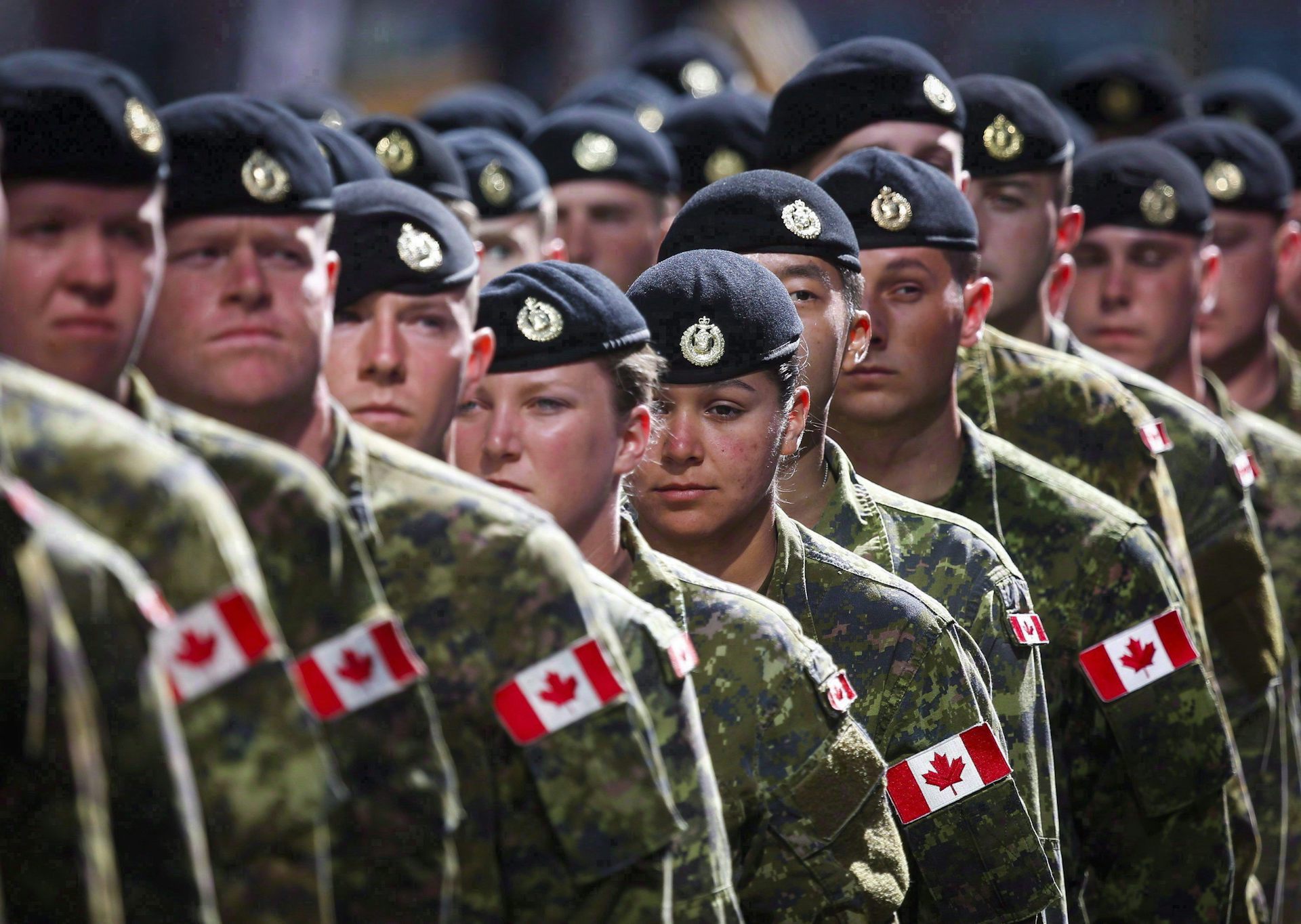 A long line of people in green army uniform and black berets. Canadian flags are on their shoulders