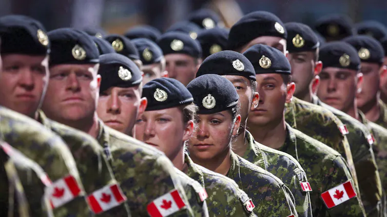 A long line of people in green army uniform and black berets. Canadian flags are on their shoulders