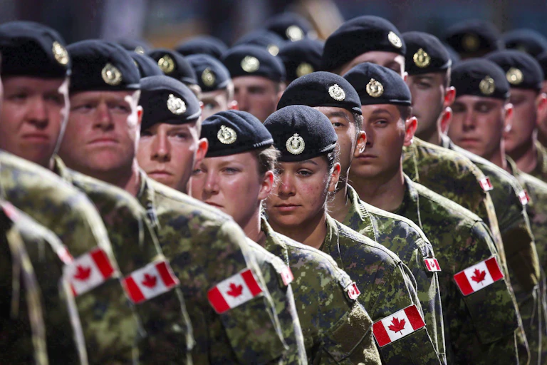 A long line of people in green army uniform and black berets. Canadian flags on their shoulders