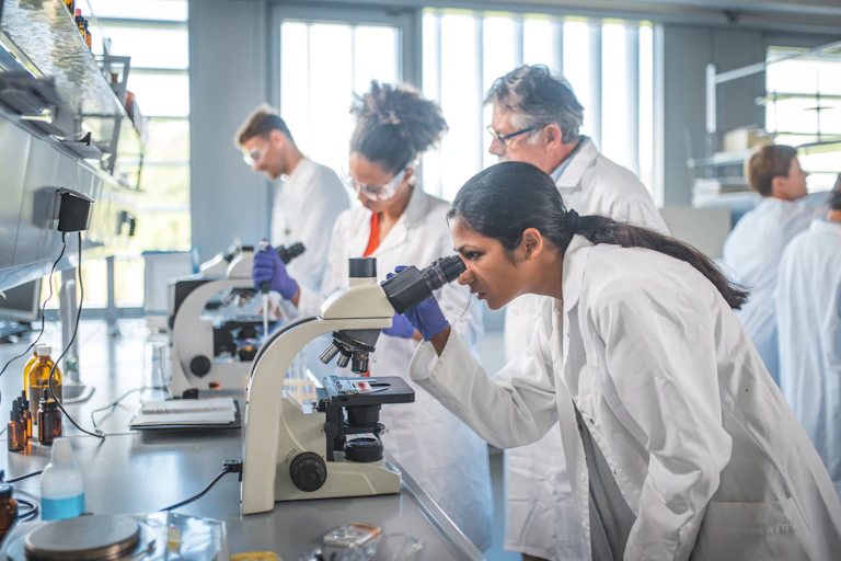 A group of scientists in lab coats working in a lab and looking through microscopes.