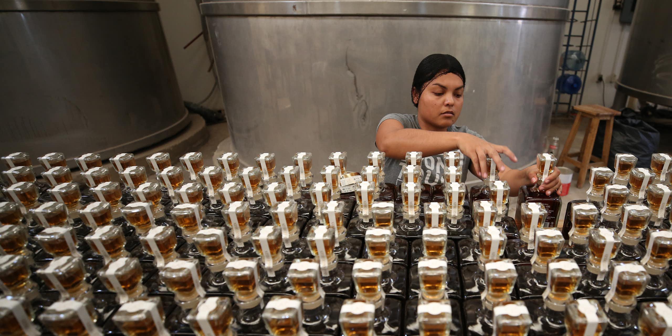 A young woman arranges bottled tequila in a factory.