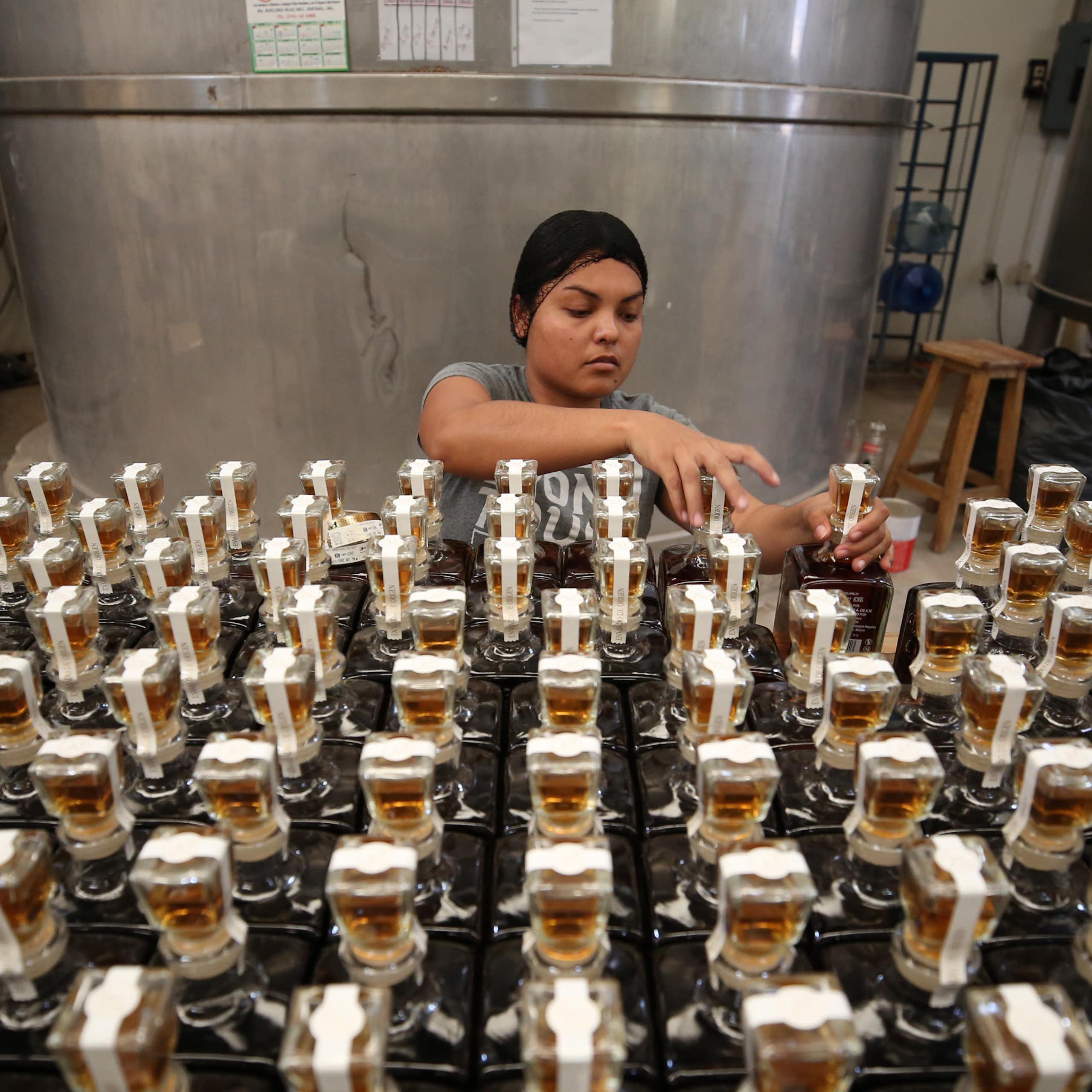 A young woman arranges bottled tequila in a factory.