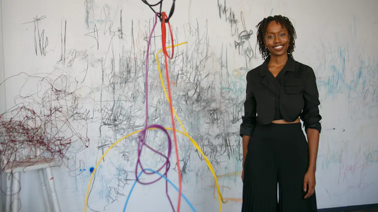 A young African woman smiles as she stands next to a vast drawing.