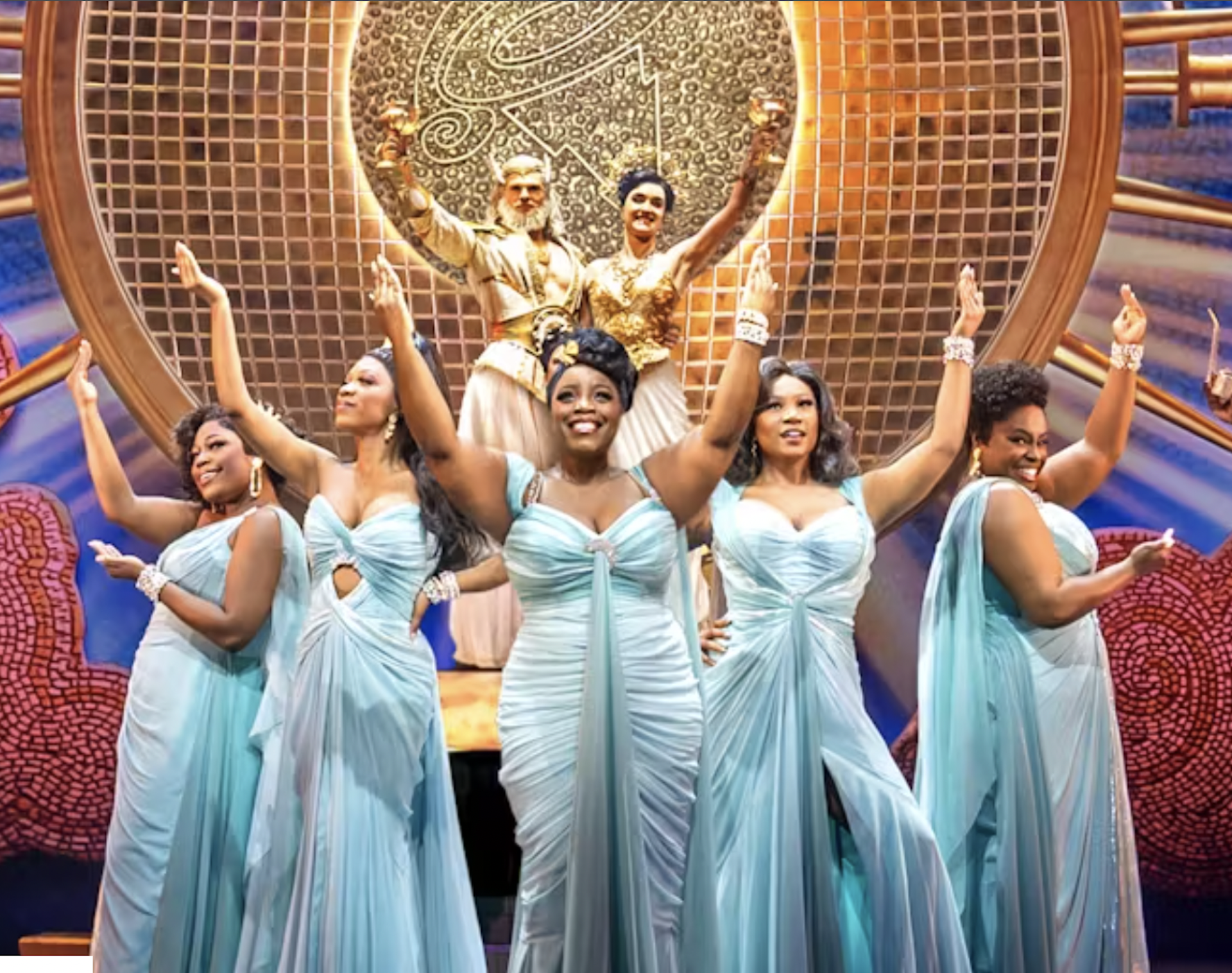 Five women singing on stage looking very glamorous in fancy frocks.
