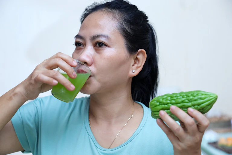 Woman holding a glass filled with bitter melon juice and whole bitter gourd