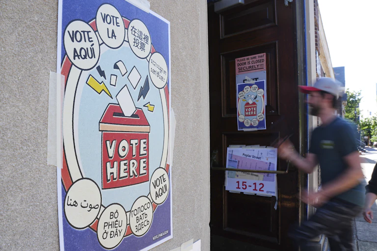 Man in T-shirt and baseball cap entered building with sign that says 'Vote Here.'
