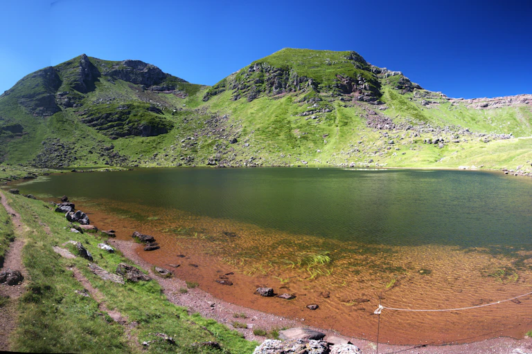 Un lac de haute montagne, dont les eaux verdissent, entouré d'herbe et de roche.