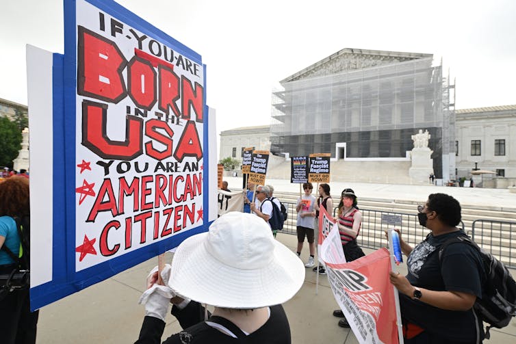 Protesters hold signs in front of a federal building.