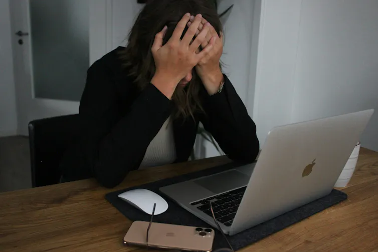 A woman sits at a desk with her head in her hands