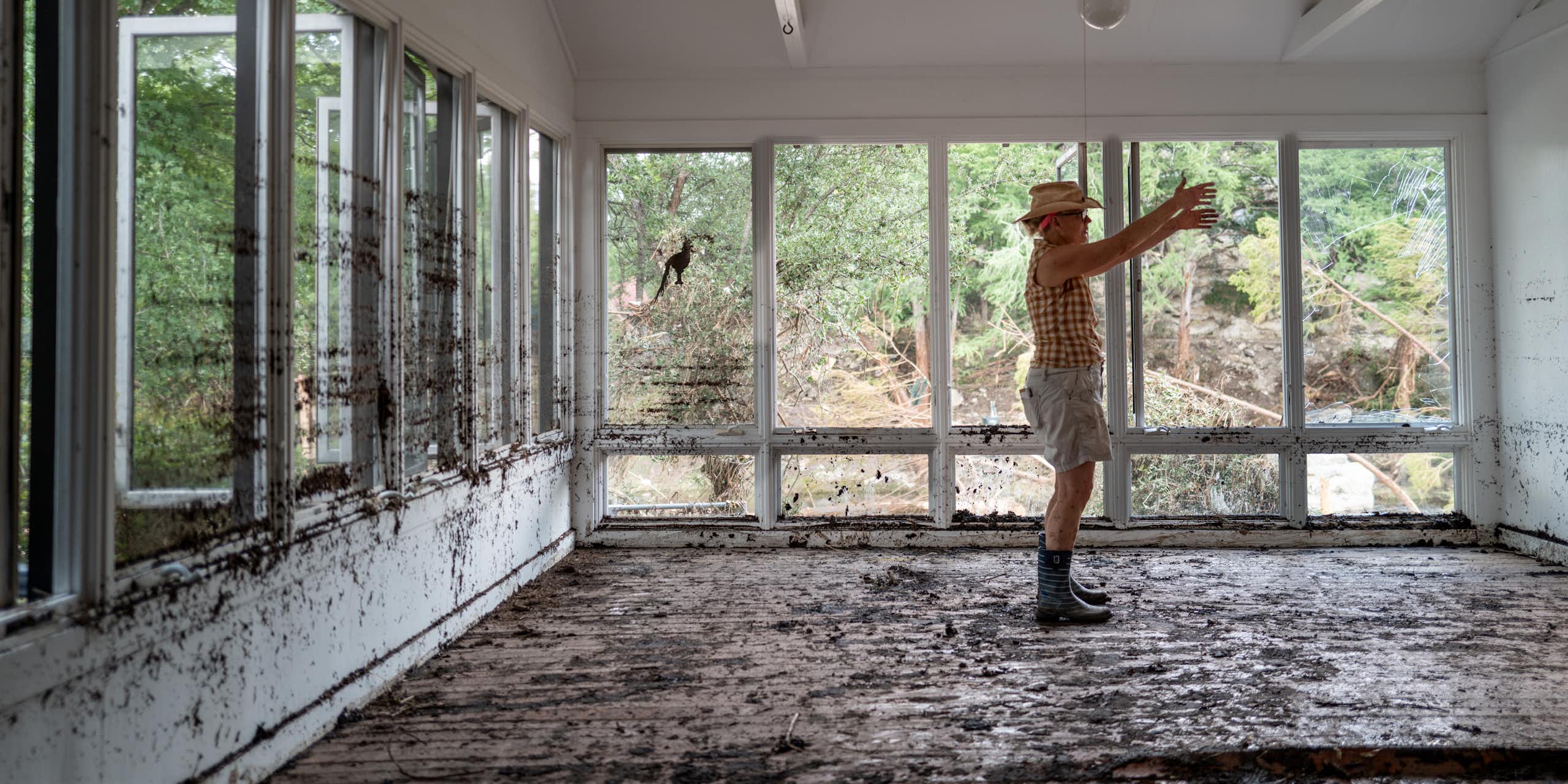 Nancy Callery walks through her childhood home while salvaging belongings after the flood. She's standing in a room with a ceiling fan and lots of windows.