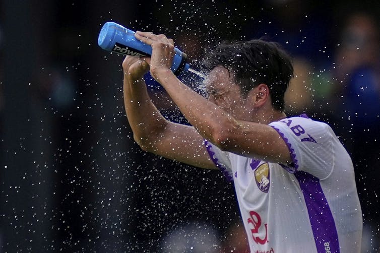 A sweating soccer player squirts water from a bottle onto his forehead during a match.