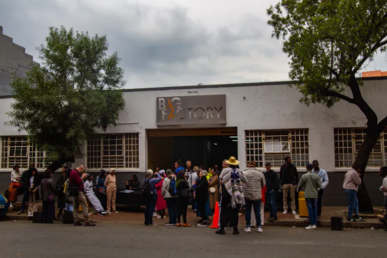 People stand and mingle outside a flat-roofed urban structure.