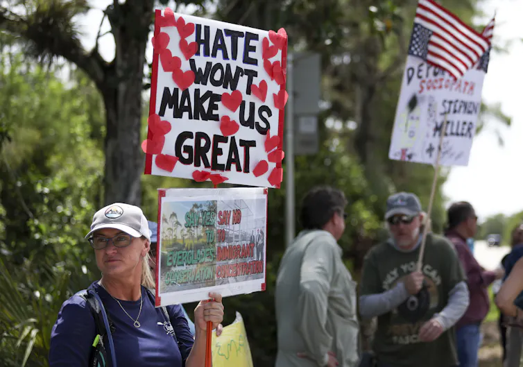 A protester in a white ball cap holds a sign reading Hate Won't Make us Great.