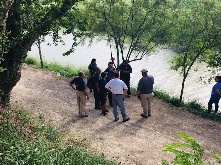 A group of men stand next to a river bank.