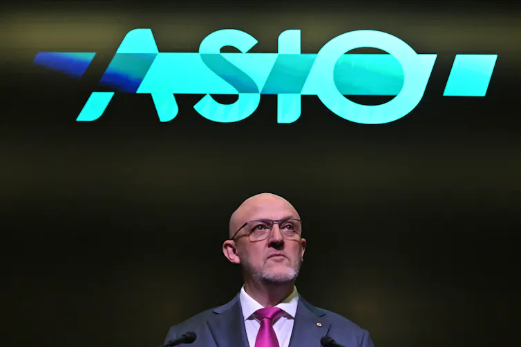 Mike Burgess standing under an illuminated ASIO sign