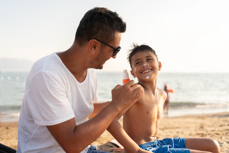 Smiling man in a t-shirt hands sunscreen to a laughing boy on a beach
