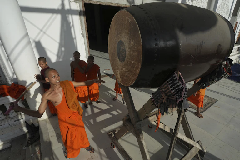 A Buddhist monk dressed in orange garments beats a giant drum at a pagoda