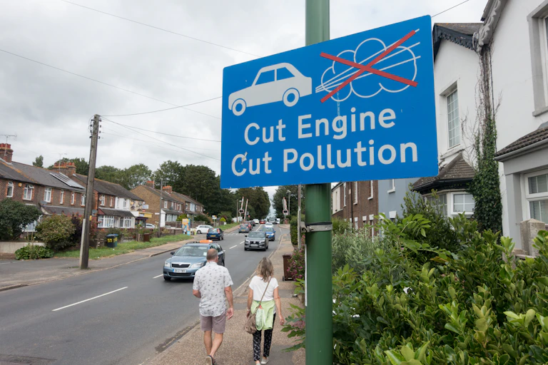 blue road sign says cut engine, cut pollution, street with people walking in background, clean air