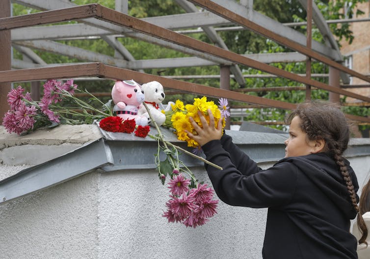 A young girl puts flowers on a building that has been destroyed by Russian bombardment.