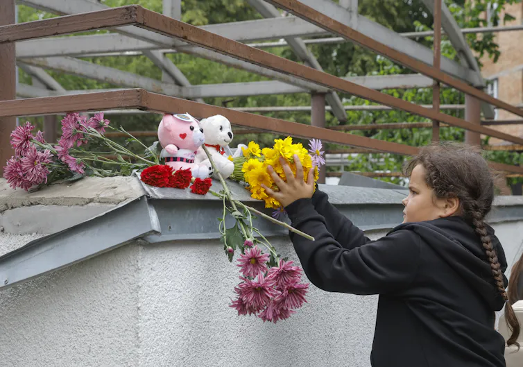 A young girl puts flowers on a building that has been destroyed by Russian bombardment.
