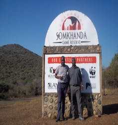 Two men stand outside in front of a sign saying Somkhanda Game Reserve