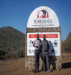 Two men stand outside in front of a sign saying Somkhanda Game Reserve
