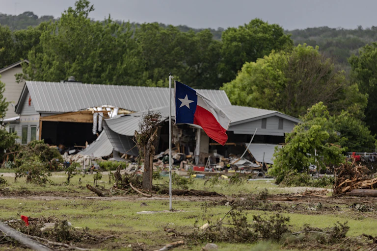 A Texas state flag flies in a yard filled with debris on July 6, 2025 in Hunt, Texas. Heavy rainfall caused flooding along the Guadalupe River in central Texas