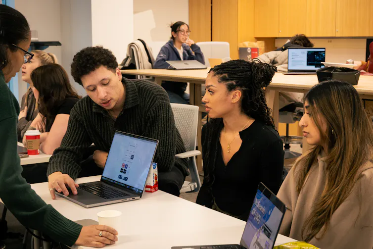 adult students sit at a desk with computer screens facing out.