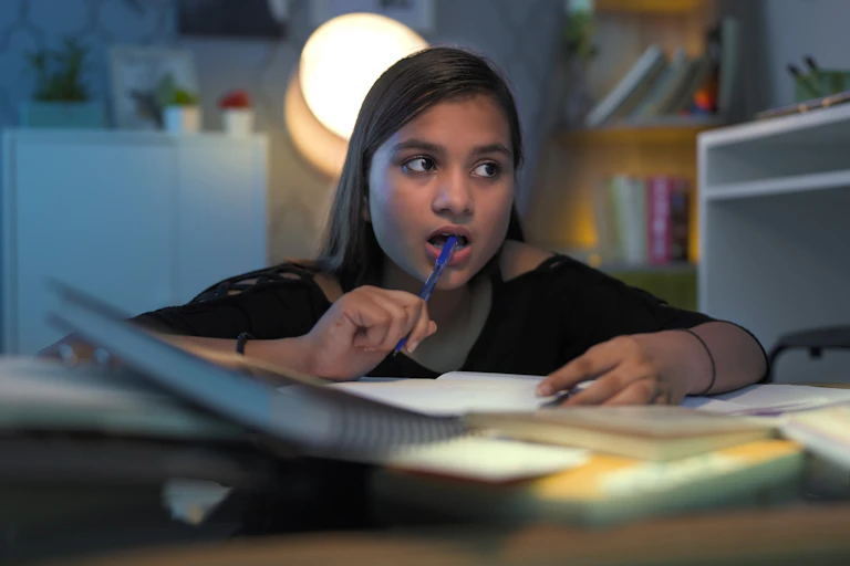 Una niña con gesto de intentar recordar algo mientras estudia en su habitación