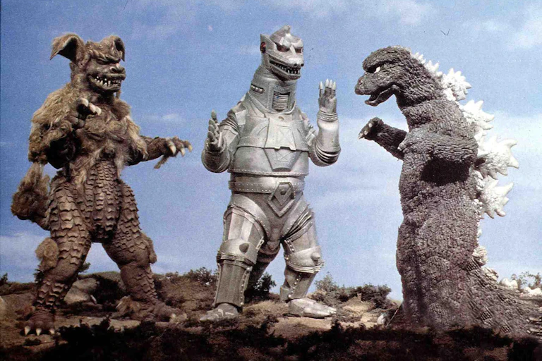 A fake monster figure stands next to a similar looking one but made of metal, and a third odd creature stands nearby.