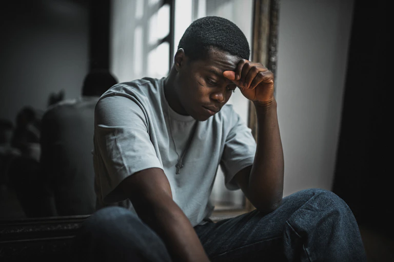 Young Black man sits while resting forehead on hand and looking stressed.