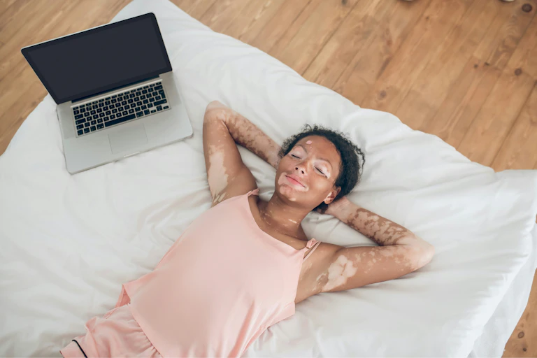 a woman lies in bed next to a laptop