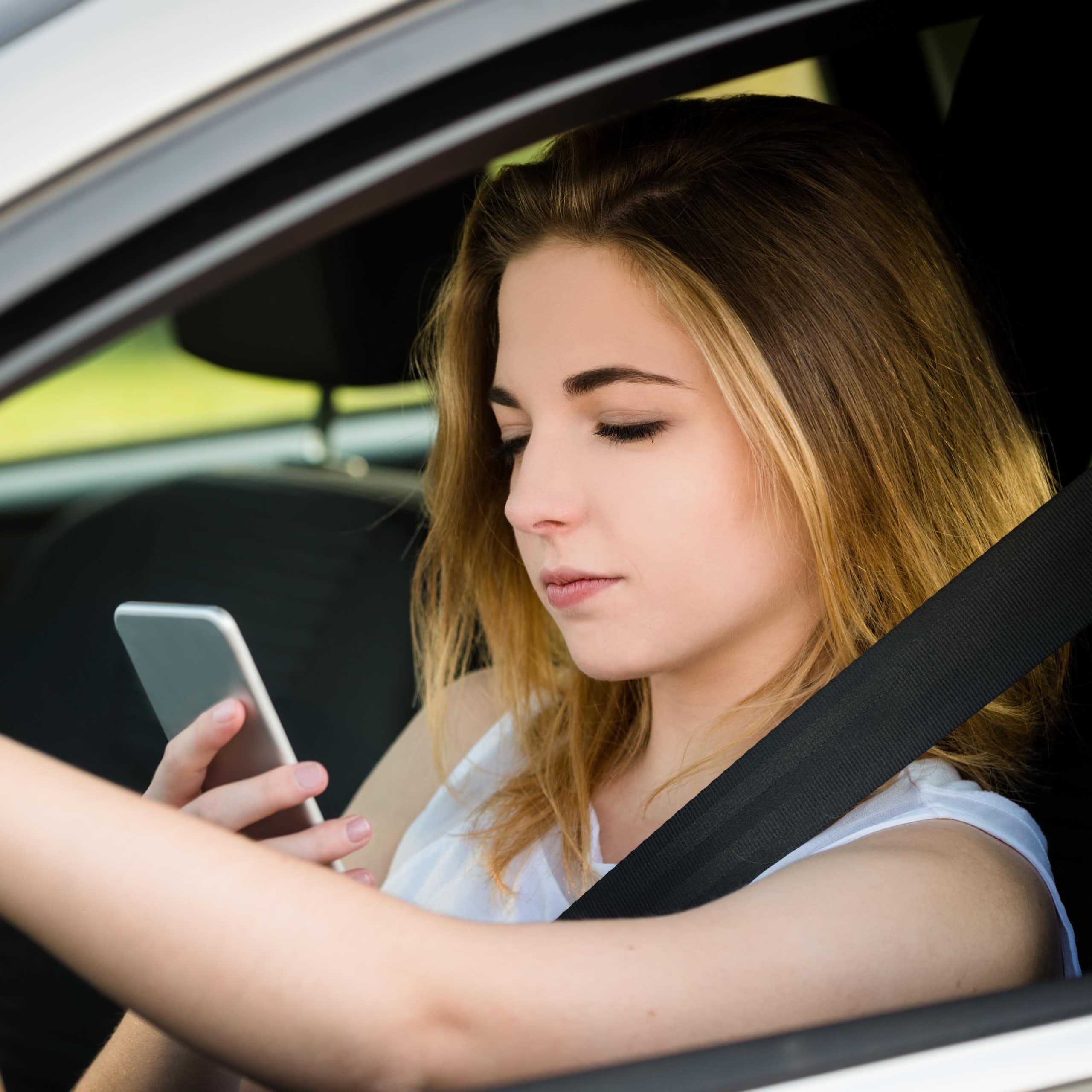 A young woman looks at her phone while driving a car.
