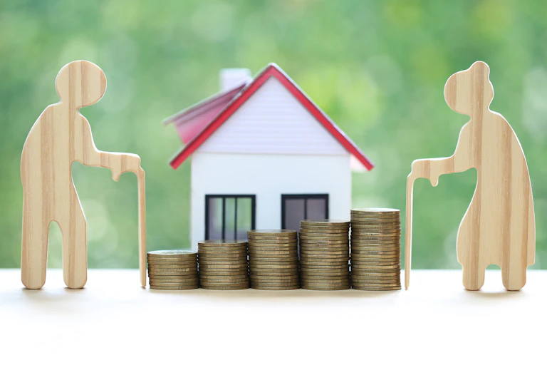 Cutout of elderly couple next to a house and stack of coins.
