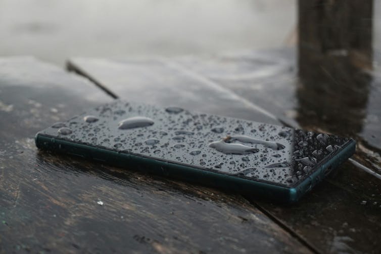Një smartphone jashtë në një tryezë me ujë që rrjedh në ekranin e tij.