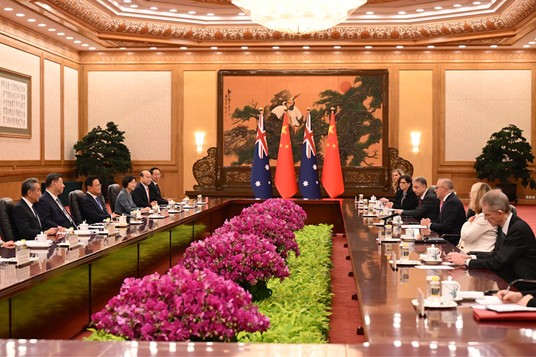 Two large long tables lined with people with Australian and Chinese flags in the background